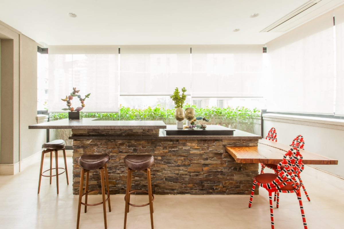 Multifuncional, o bar, com espaço para preparos e para refeições, conta com um mix elegante de materiais, projetado com tampo de café imperial ferrogado com frontão de pedra esculpida